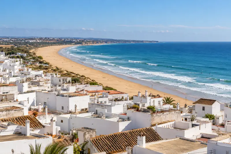 La playa larga y dorada de Conil vista desde lo alto del pueblo, con las azoteas blancas en primer plano